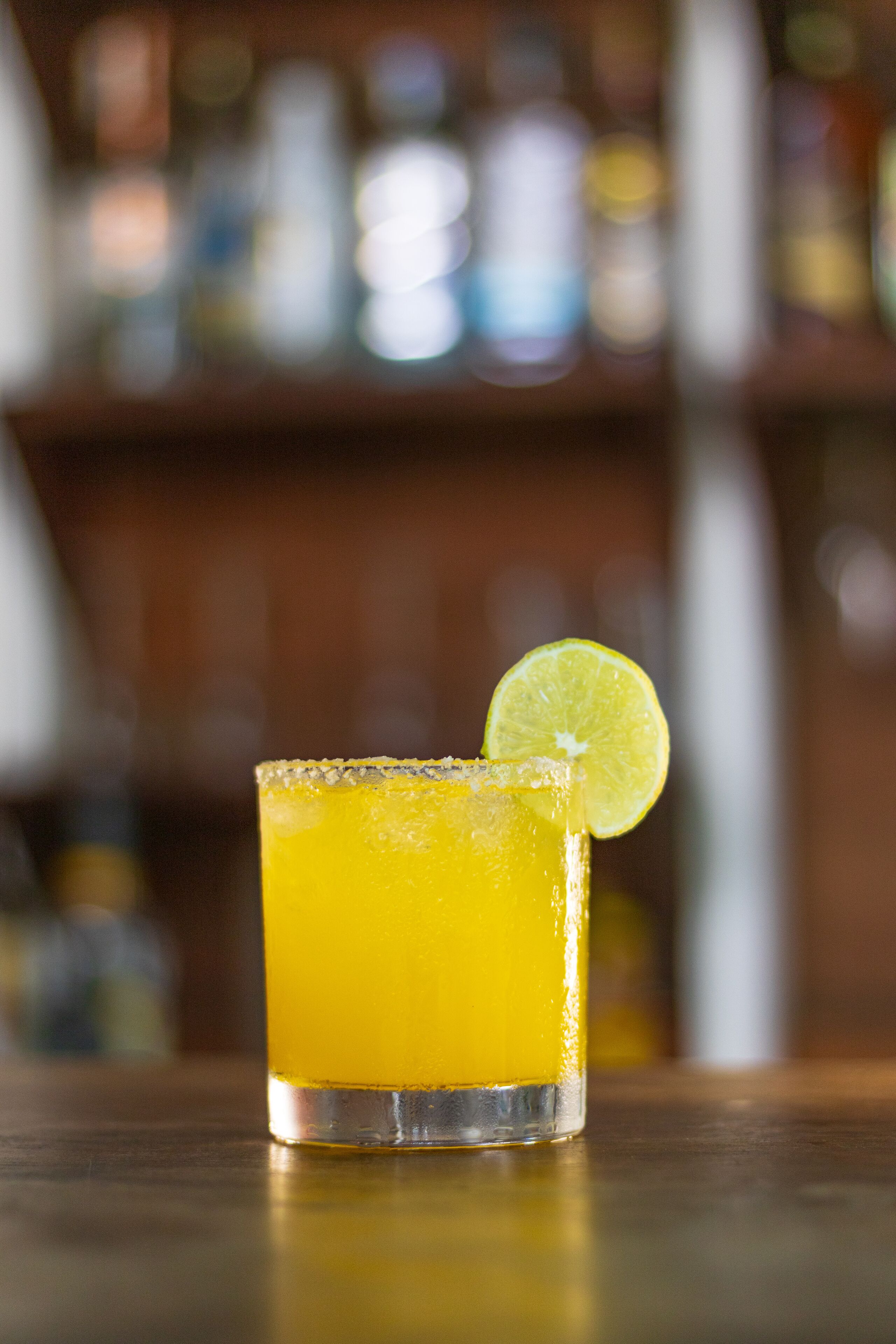 Ein Glas gelbes Getränk mit einer Limettenscheibe auf einer Holztischplatte.