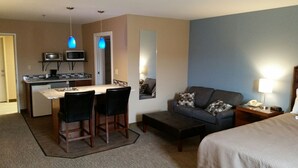A hotel room with a kitchenette, a sofa, a bed, and a small table with a lamp. - Rock Creek Hotel (Sabetha)