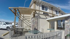 A covered outdoor area with a wooden deck, stone pillars, and glass tables. - Rock Creek Hotel (Sabetha)