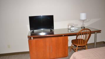 A hotel room with a wooden desk, a television, a lamp, and a chair.