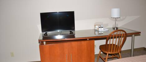 Una habitación de hotel con un escritorio de madera, un televisor, una lámpara y una silla.