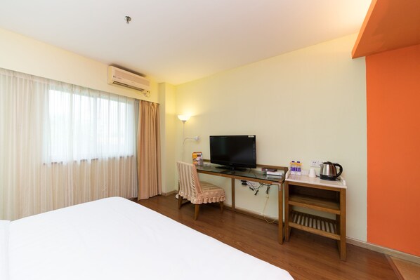 Una habitación de hotel con una cama, un escritorio con televisor, una silla y una mesita con hervidor y tazas.