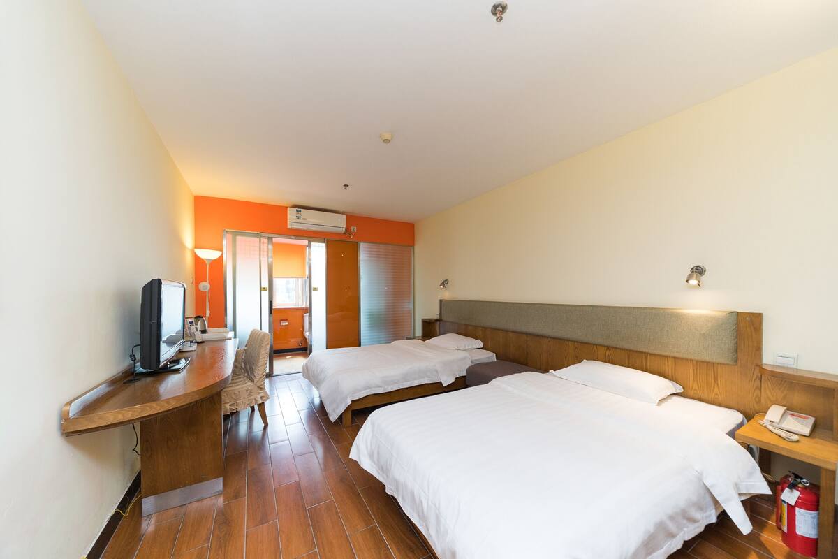 A hotel room with two beds, a desk with a computer, a chair, and a telephone.