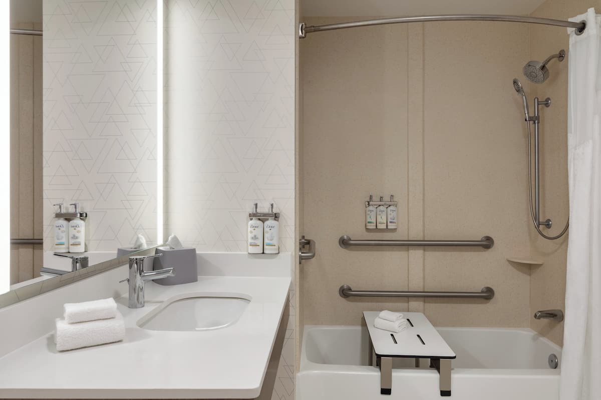 A modern bathroom with two sinks, a bathtub, and a shower with grab bars.