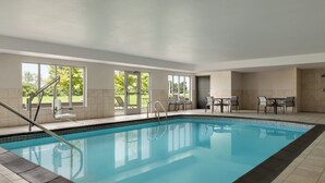 An indoor swimming pool with clear glass walls, a tiled floor, and a seating area with tables and chairs. - Holiday Inn Express Hotel & Suites NORTH FREMONT by IHG (Fremont)