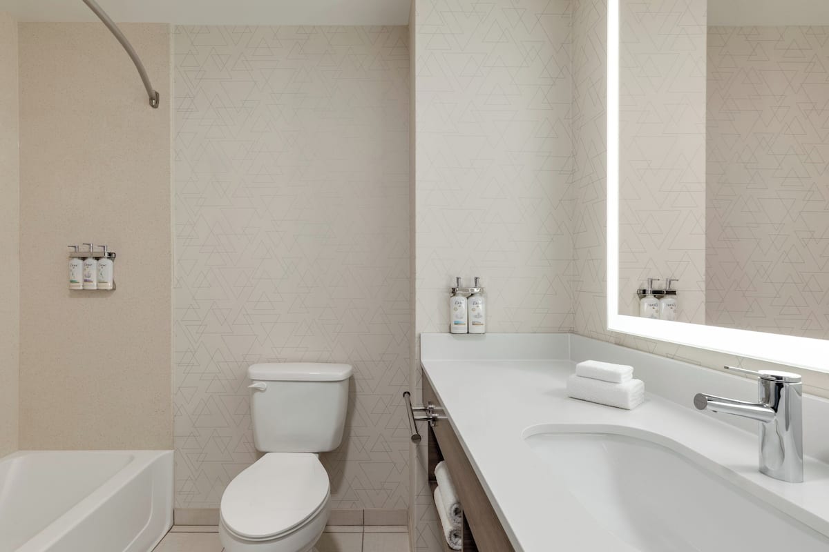 A modern bathroom with a toilet, bathtub, and a large mirror above the sink.