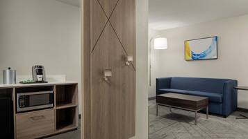 A modern hotel room with a kitchenette, a blue sofa, a coffee table, and a contemporary abstract painting.