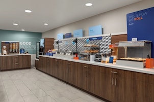 Un área de desayuno moderna con una barra que exhibe diversos alimentos y un cartel que dice 'THIS IS HOW WE ROLL'.