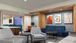 A modern hotel lobby with a reception desk, seating area, and artwork. - Holiday Inn Express Hotel & Suites NORTH FREMONT by IHG (Fremont)