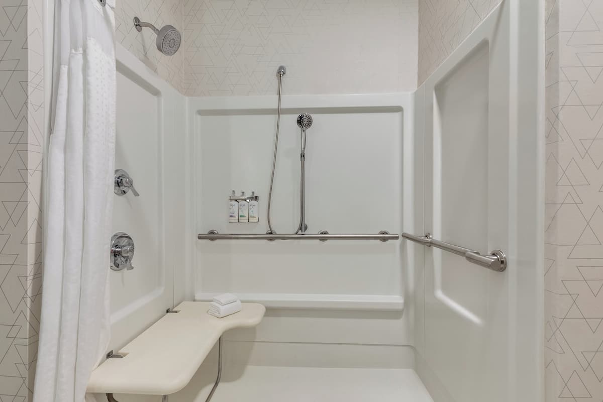 A white, walk-in shower with a bench, handheld showerhead, and a handheld faucet.