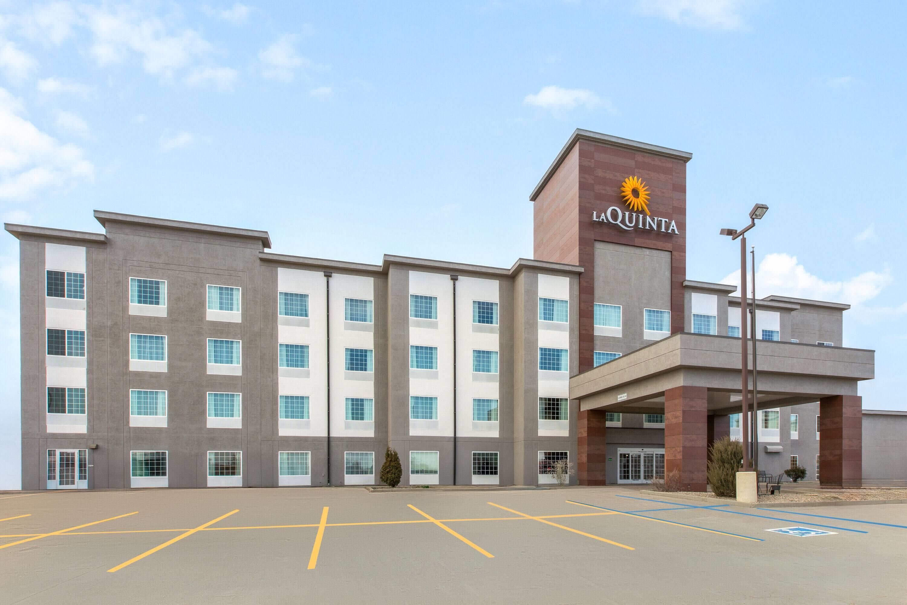 Un hotel dal design moderno, con un cartello ben visibile 'La Quinta', un parcheggio con posti delimitati e un ingresso coperto.