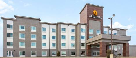 Un hotel de diseño moderno, con un llamativo letrero de 'La Quinta', un estacionamiento con espacios delimitados y una entrada cubierta.
