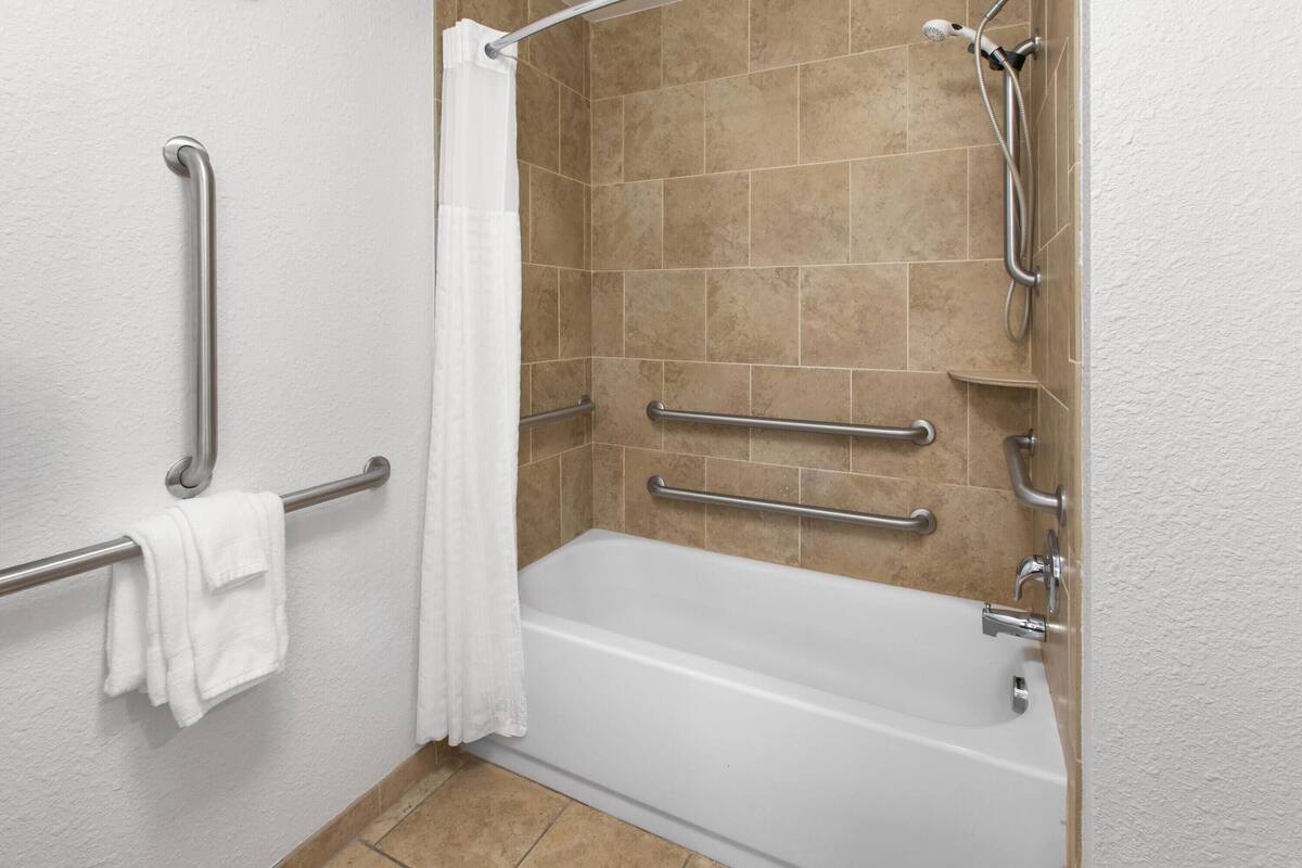 Un baño con bañera, barras de apoyo, cabezal de ducha y toallero.