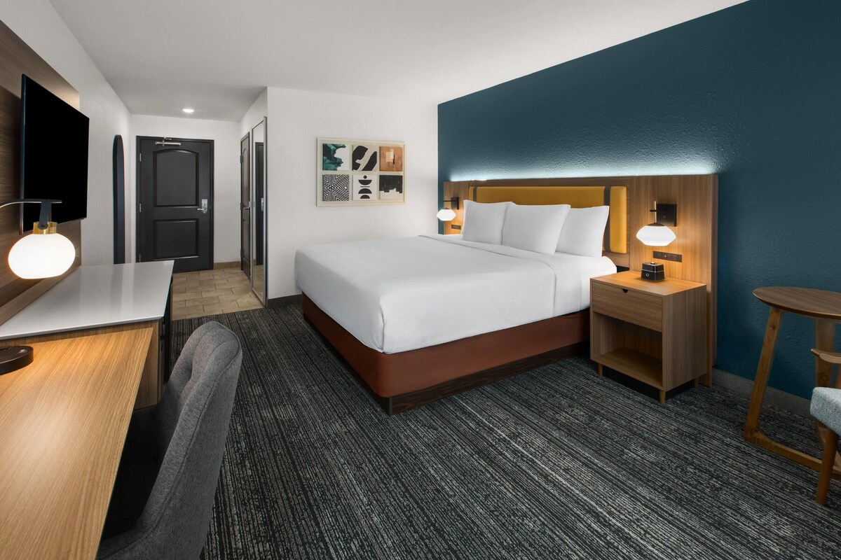 A hotel room with a bed, bedside tables, a desk, and a chair.