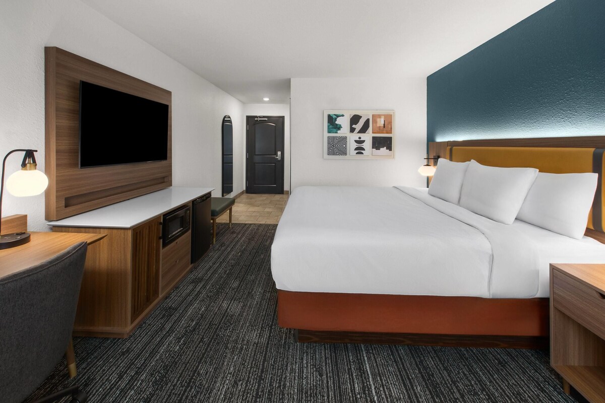 Una habitación de hotel con cama, escritorio, televisor y obras de arte en la pared.