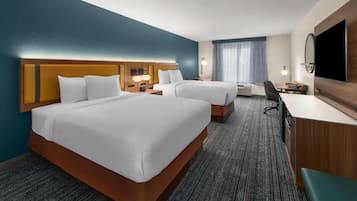 Habitación de hotel con dos camas, un escritorio, una silla, un televisor y un espejo grande.