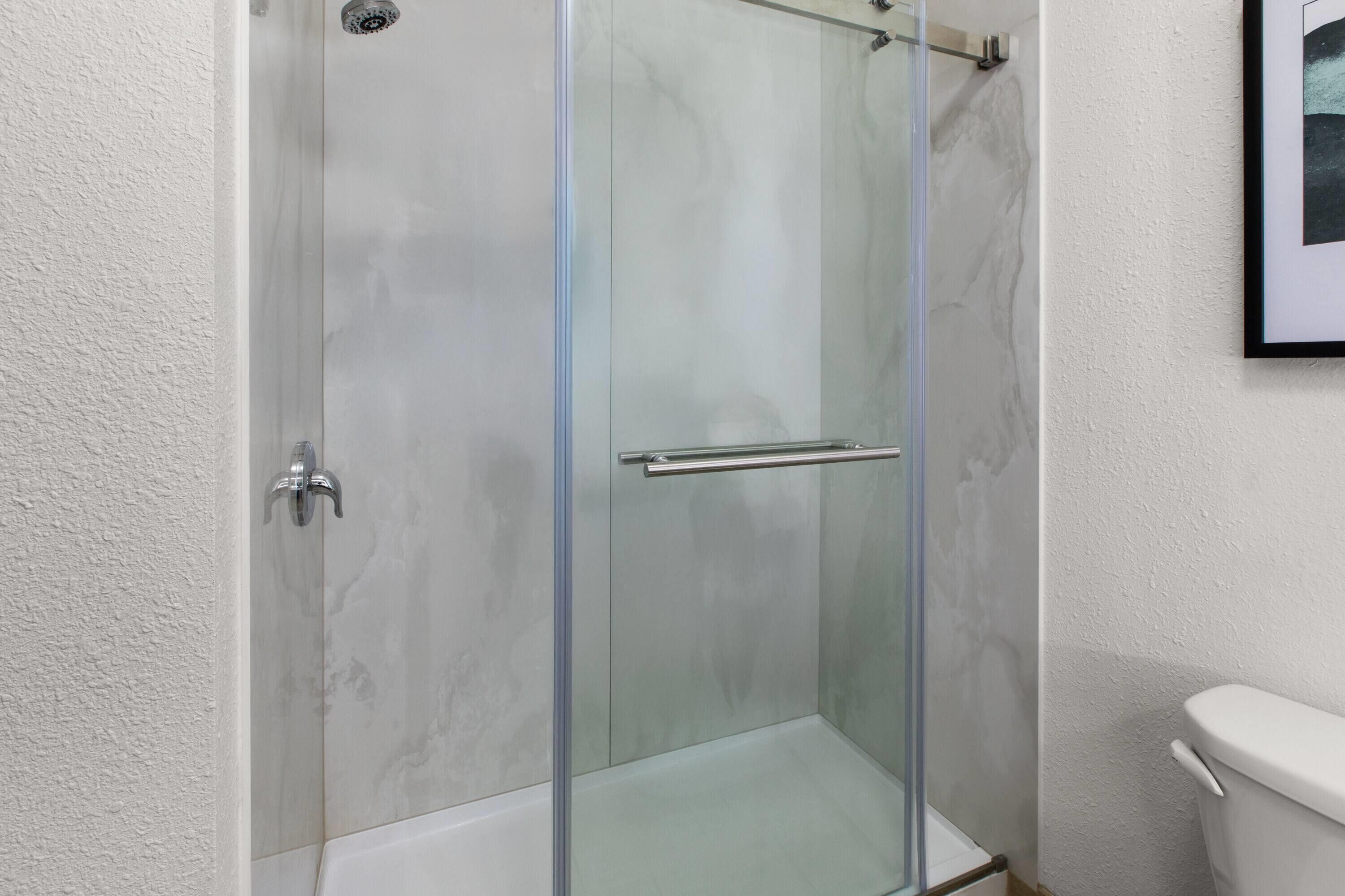 Une cabine de douche entièrement vitrée, dotée d’une porte en verre, d’une poignée en métal et d’une paroi de douche en verre.