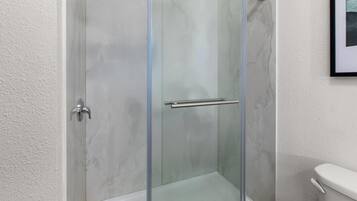 Une cabine de douche entièrement vitrée, dotée d’une porte en verre, d’une poignée en métal et d’une paroi de douche en verre.