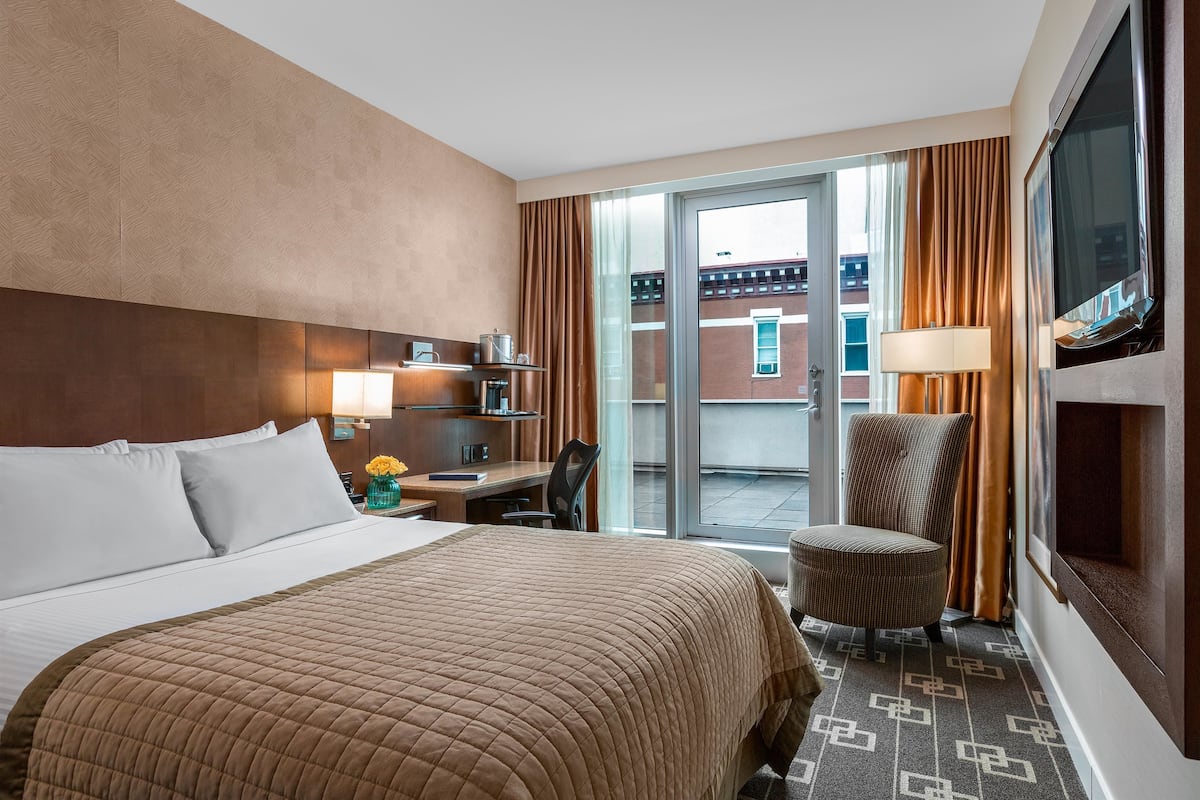 A hotel room with a large bed, a desk with a lamp, a chair, and a view of the outside.