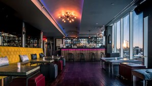 Un bar con techo alto, una barra con taburetes y una zona de estar con un banco amarillo acolchado.