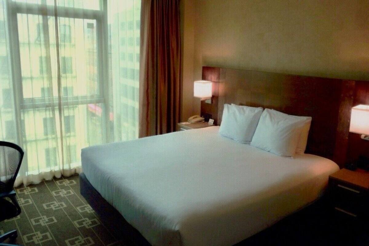 A hotel room with a large bed, a nightstand with a lamp, a chair, and a window with curtains.
