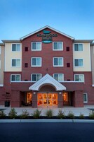 Un hotel de varios pisos con fachada de ladrillo, una entrada central con arco blanco y un cartel que indica que es un Homewood Suites Hilton.