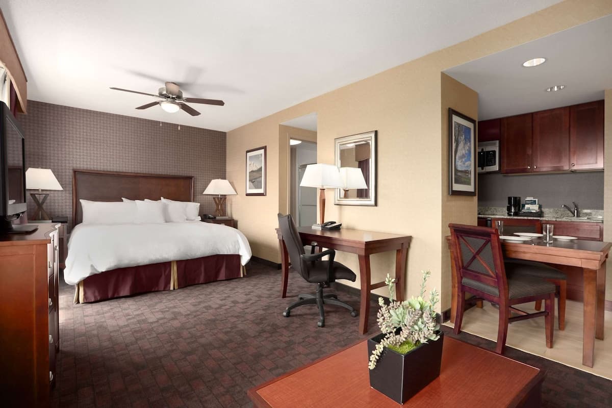 A hotel room with a bed, desk, chair, and kitchenette.