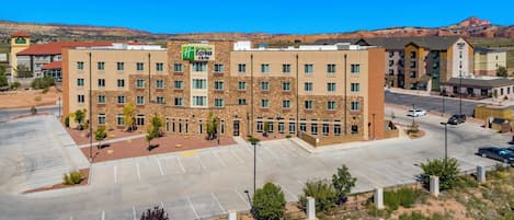 A multi-story hotel with a stone facade, a parking lot, and a view of the surrounding landscape.