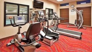 Une salle de sport équipée de tapis de course, de vélos elliptiques et d’un vélo d’appartement, avec un sol recouvert d’une moquette rouge et une horloge au mur.