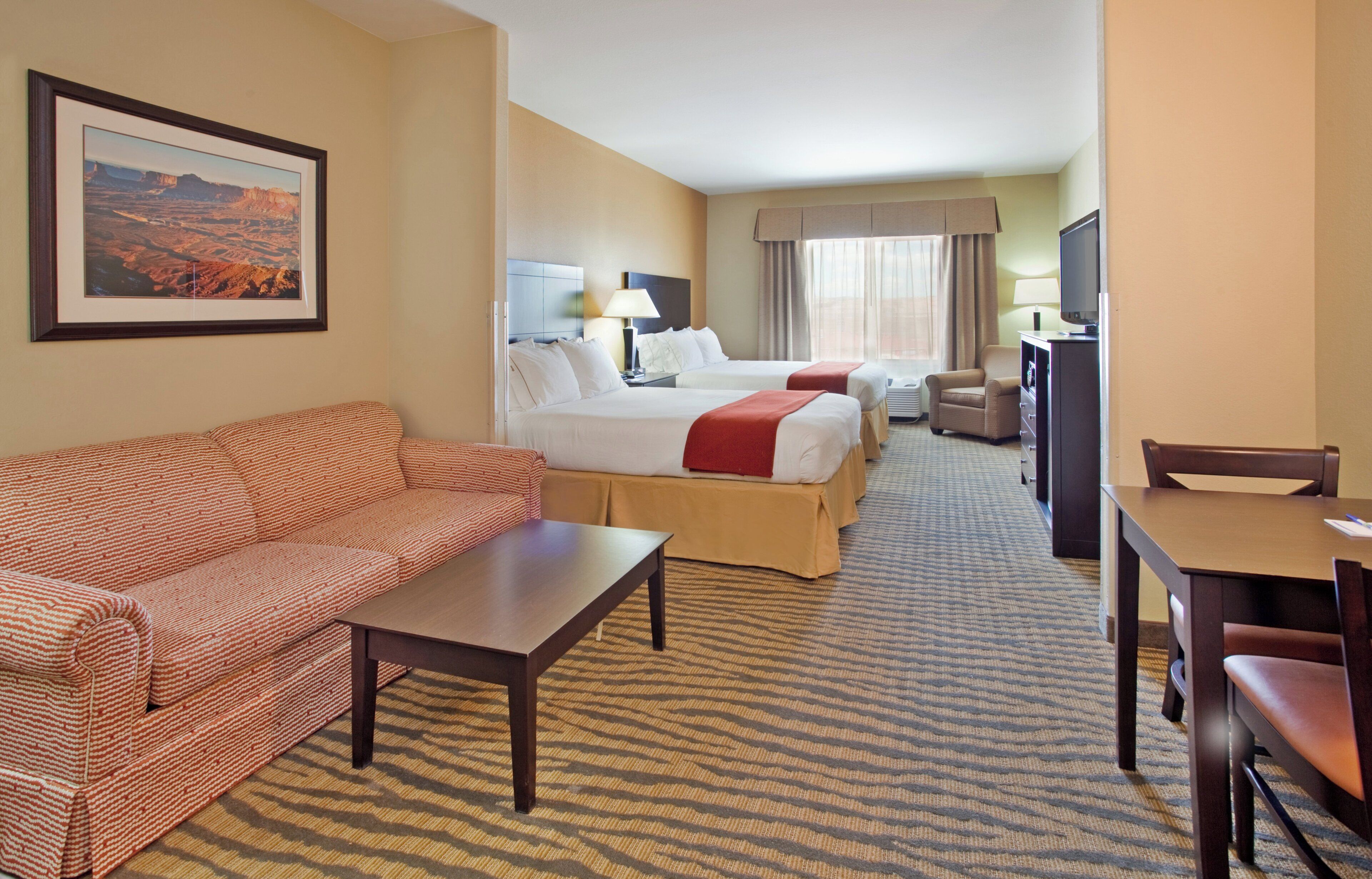 A hotel room with a sofa, two beds, a TV, and a desk.