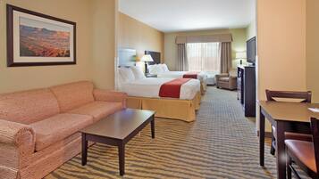 A hotel room with a sofa, two beds, a TV, and a desk.