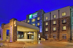 Um hotel Holiday Inn Express & Suites com fachada de pedra, entrada coberta e exterior bem iluminado.