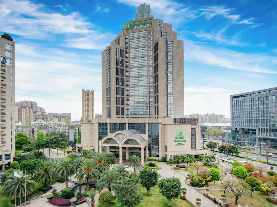 Un edificio de gran altura con el logotipo de Holiday Inn, rodeado de vegetación exuberante y otros edificios altos.