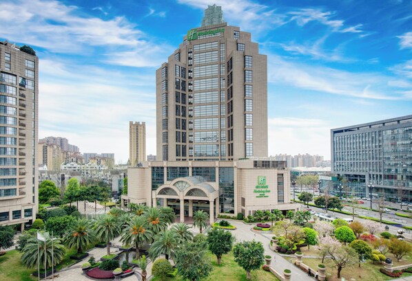 A high-rise building with a Holiday Inn sign, surrounded by lush greenery and other high-rise buildings.