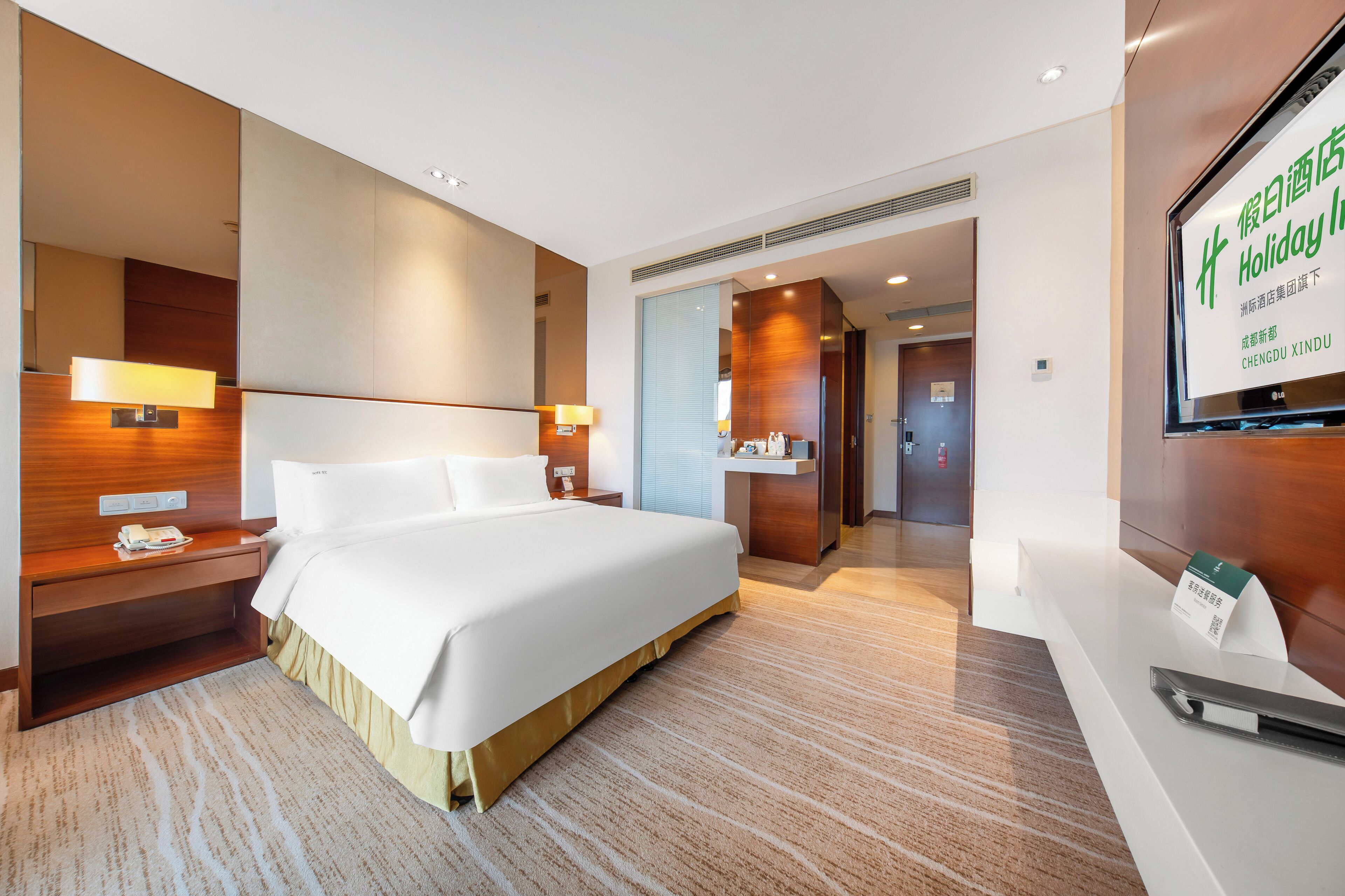 A hotel room with a large bed, bedside tables, a desk, and a television.