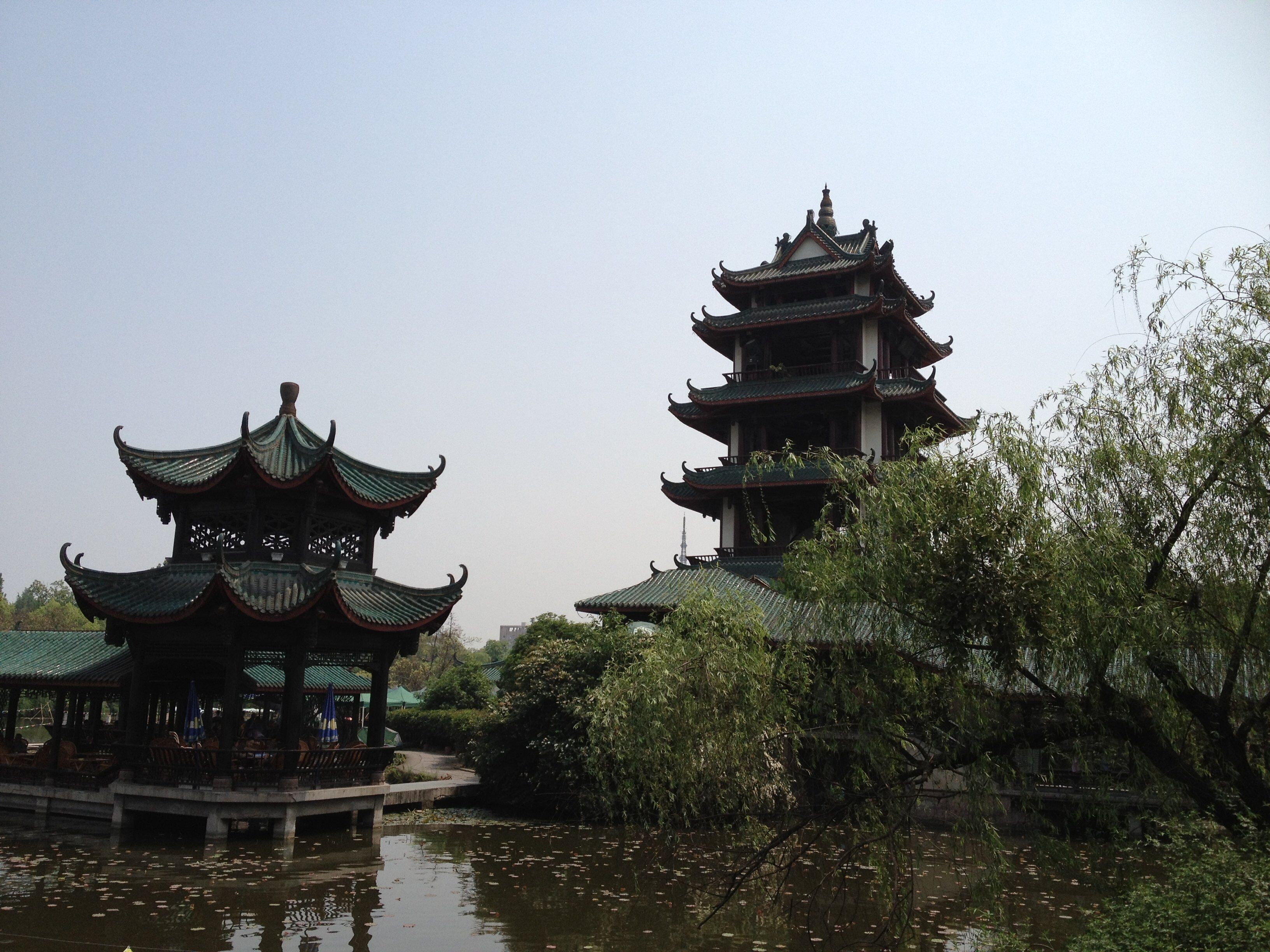 En traditionell, flervånings pagoda med en paviljong framför, omgiven av vatten och grönska.
