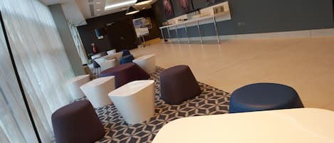 A modern hotel lobby with a patterned floor, several seating areas with round and square stools, and a reception desk.