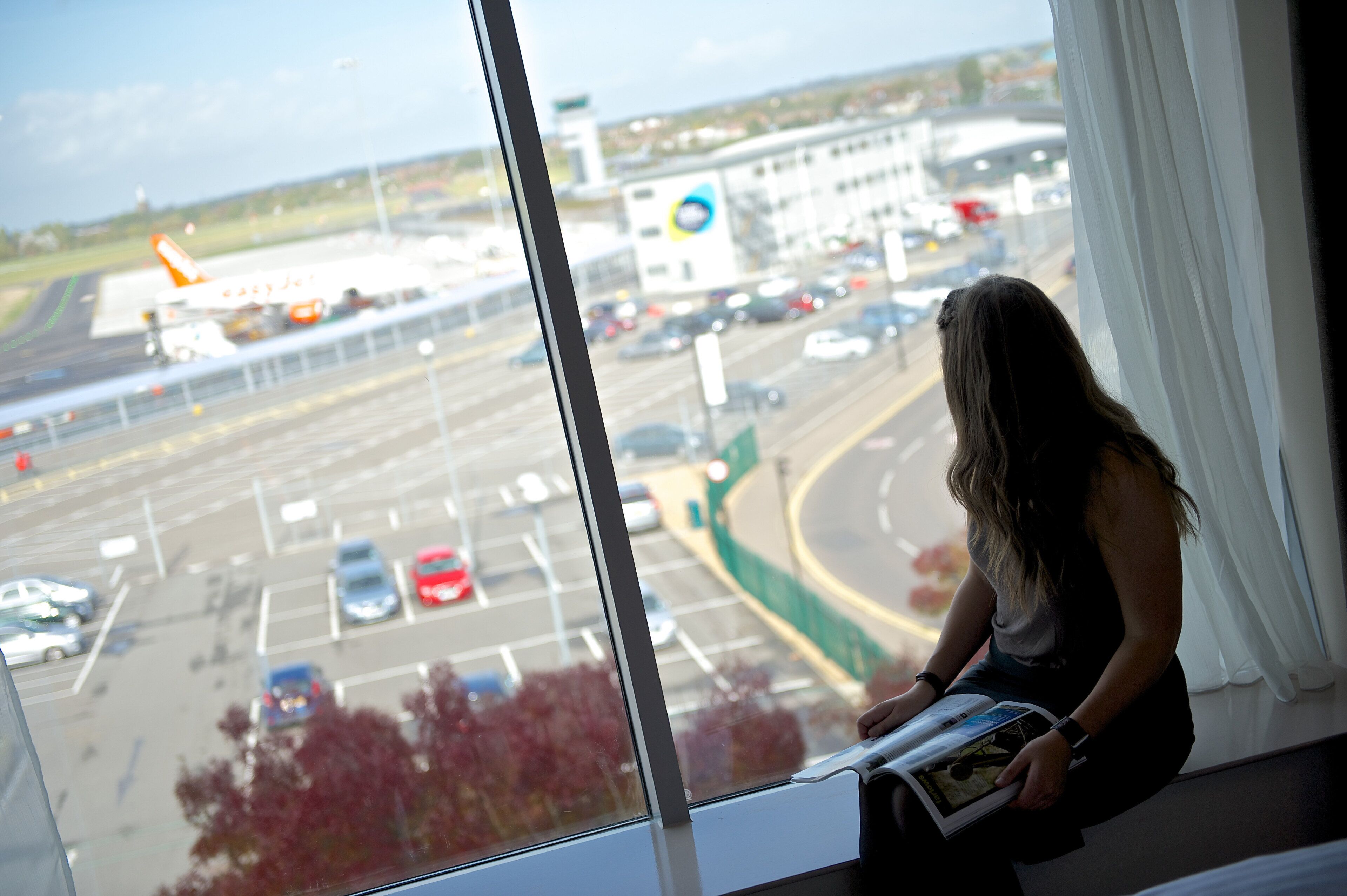 A person sitting by a window with a view of a busy road and a building with a blue logo.