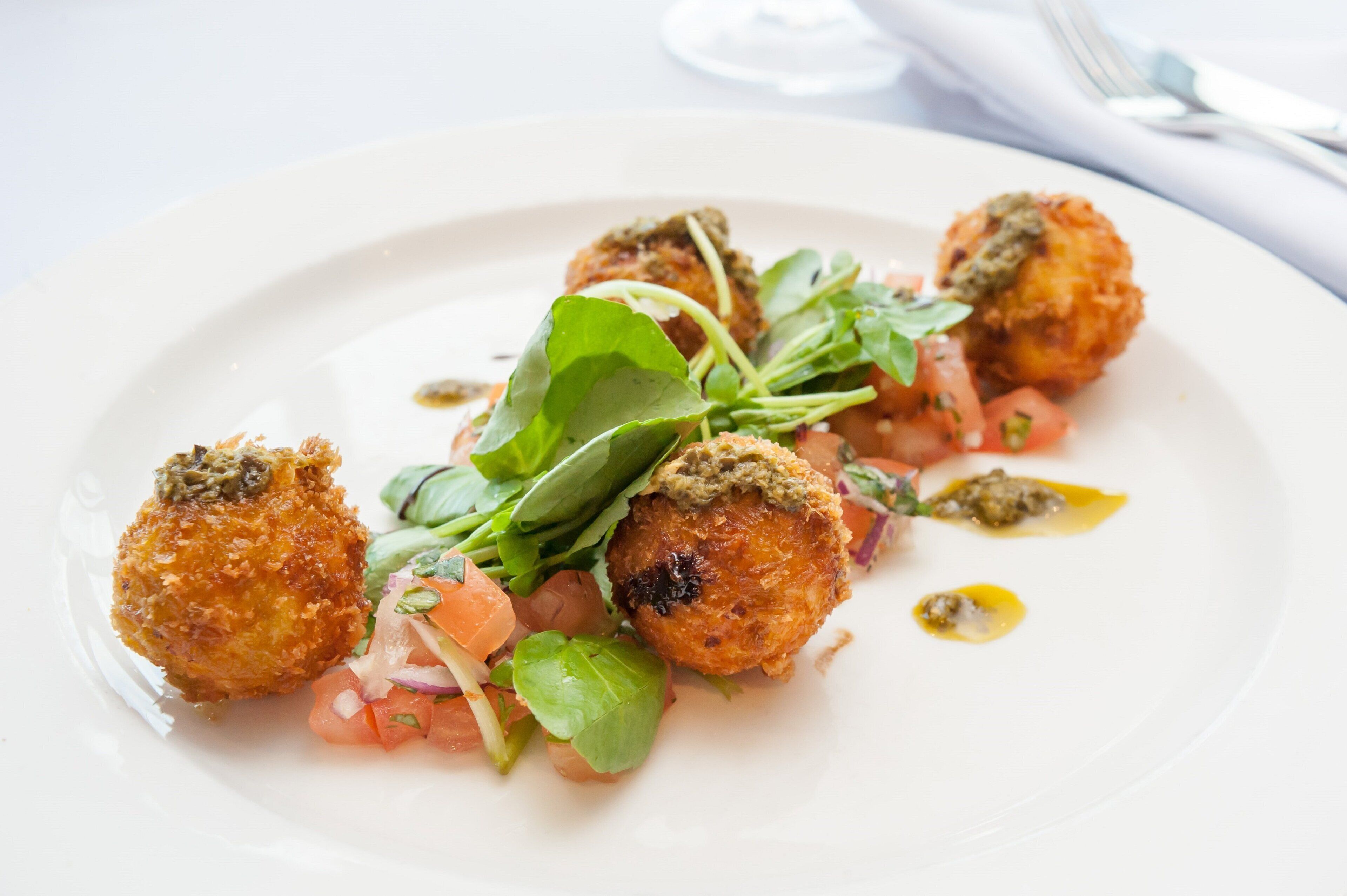 A plate of food with breaded balls, greens, and diced tomatoes.