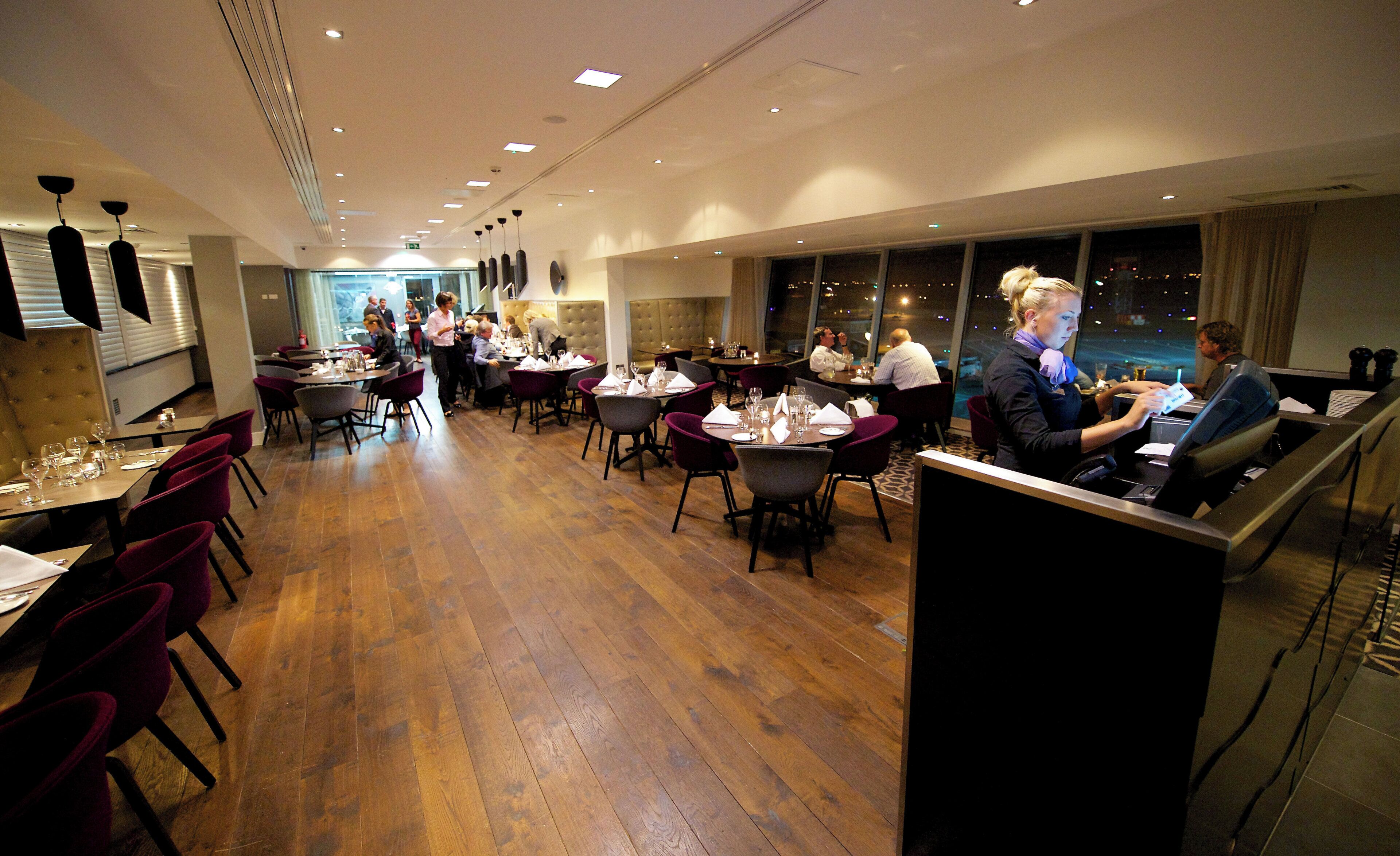 A restaurant with wooden flooring, round tables, and purple chairs.