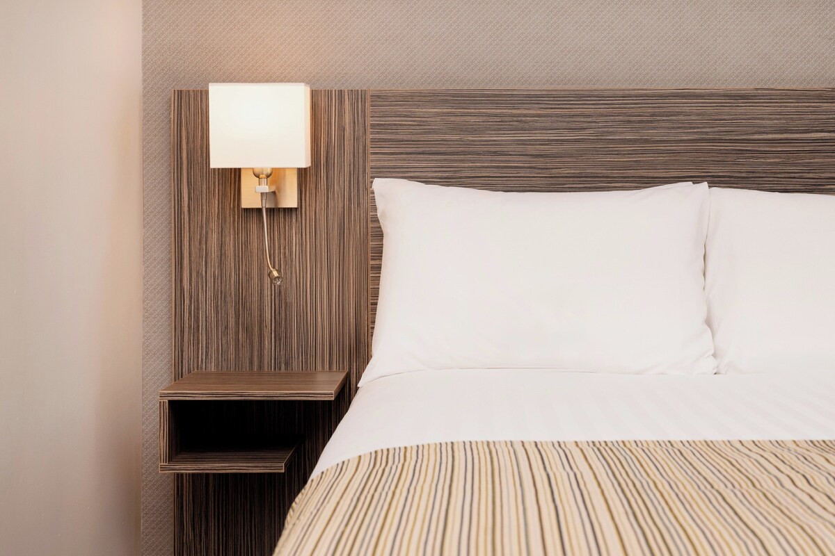 A hotel room with a large bed, a nightstand with a lamp, and a wooden headboard.