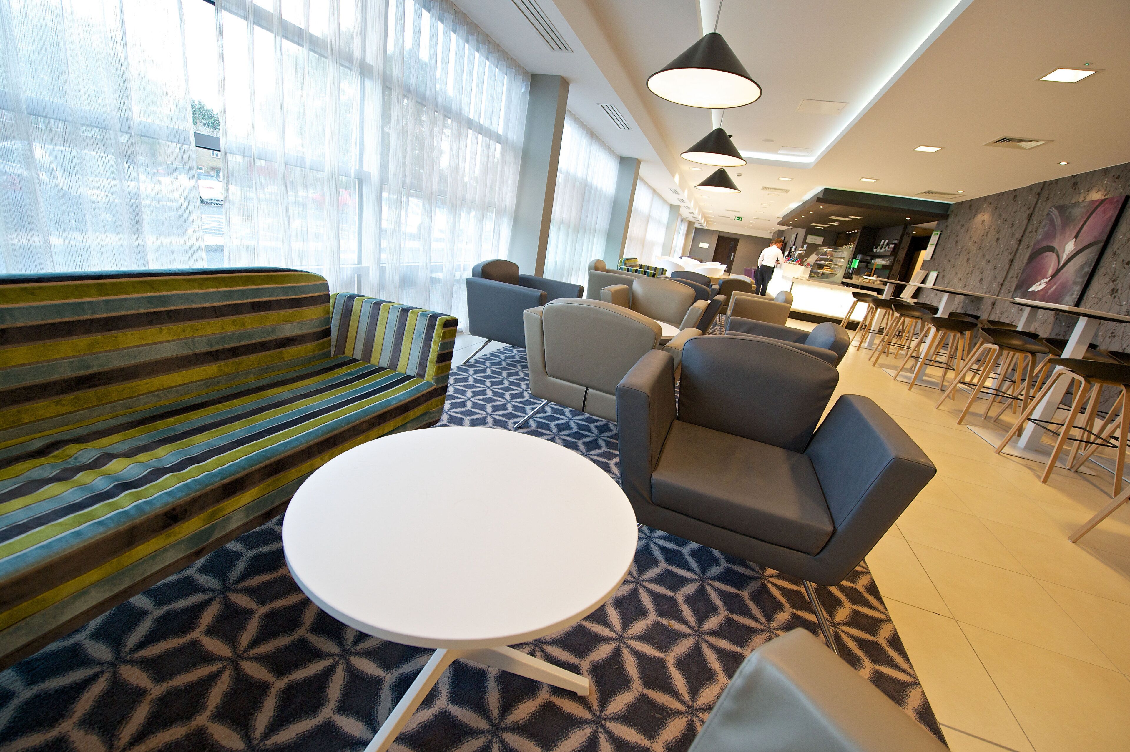 A modern lounge area with a sofa, chairs, a round table, and a bar area with stools.