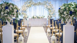A wedding ceremony aisle with white floral arrangements, a white altar, and gold chairs. - Holiday Inn Southend by IHG (Southend-on-Sea)