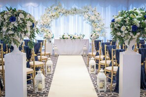A wedding ceremony aisle with white floral arrangements, a white altar, and gold chairs. - Holiday Inn Southend by IHG (Southend-on-Sea)