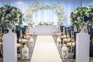 A wedding ceremony aisle with white floral arrangements, a white altar, and gold chairs.