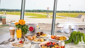 A breakfast table with pastries, fruits, and a drink, overlooking an airport runway. - Holiday Inn Southend by IHG (Southend-on-Sea)