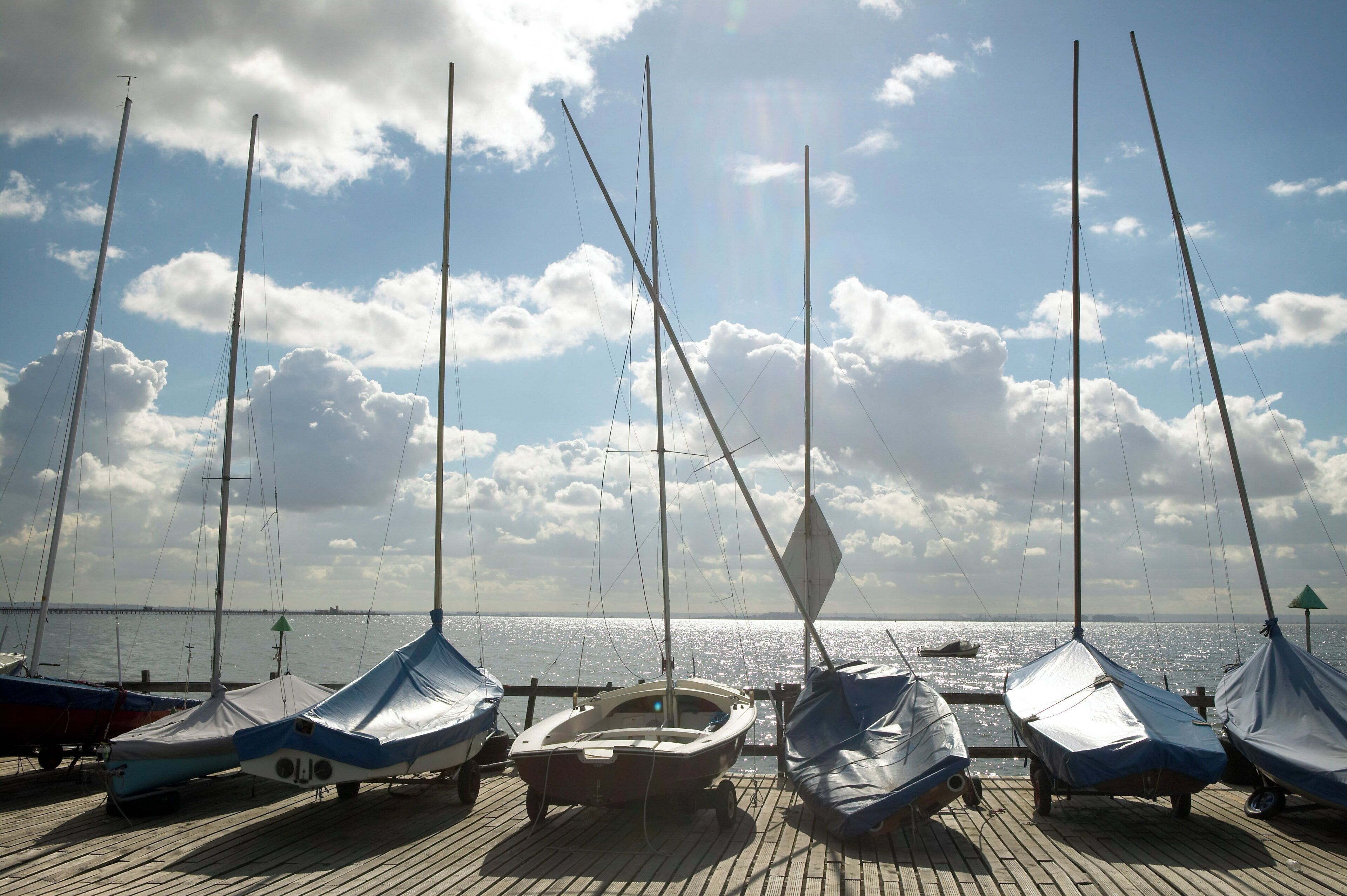 A wooden dock with covered boats and a clear sky with clouds.