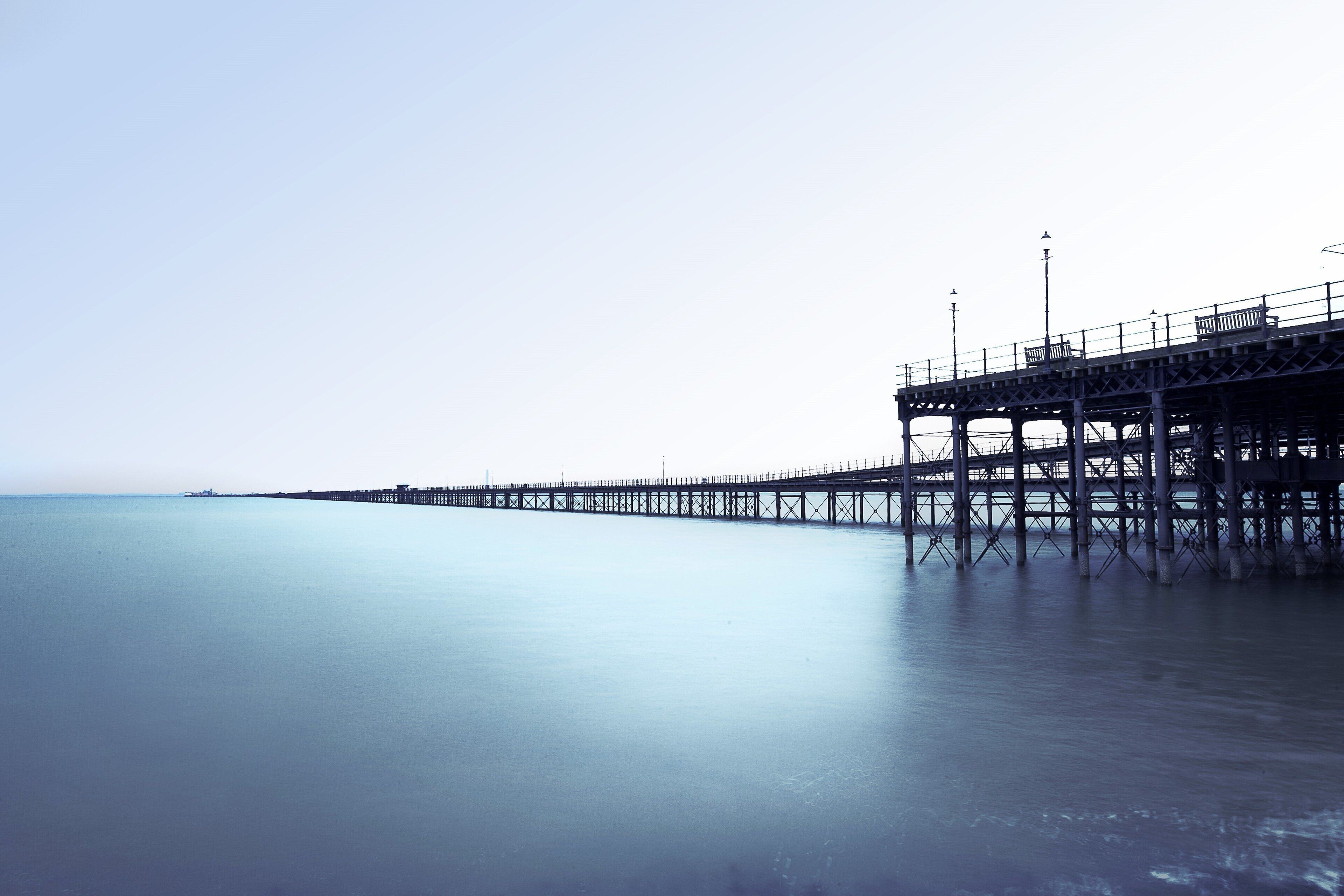 A pier extending into calm water with a clear sky.