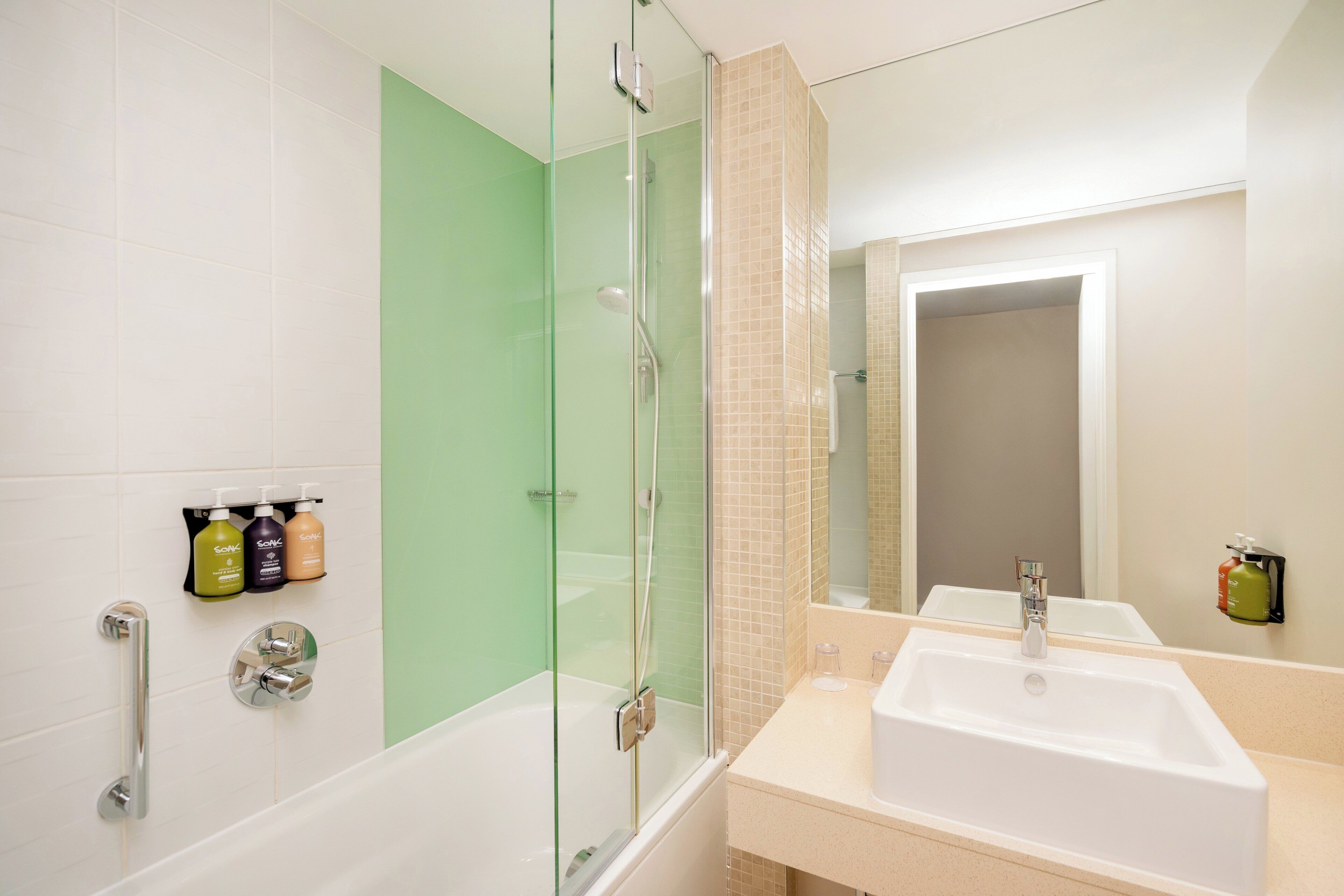 Un baño moderno con ducha de vidrio, un lavamanos blanco y un espejo sobre él.