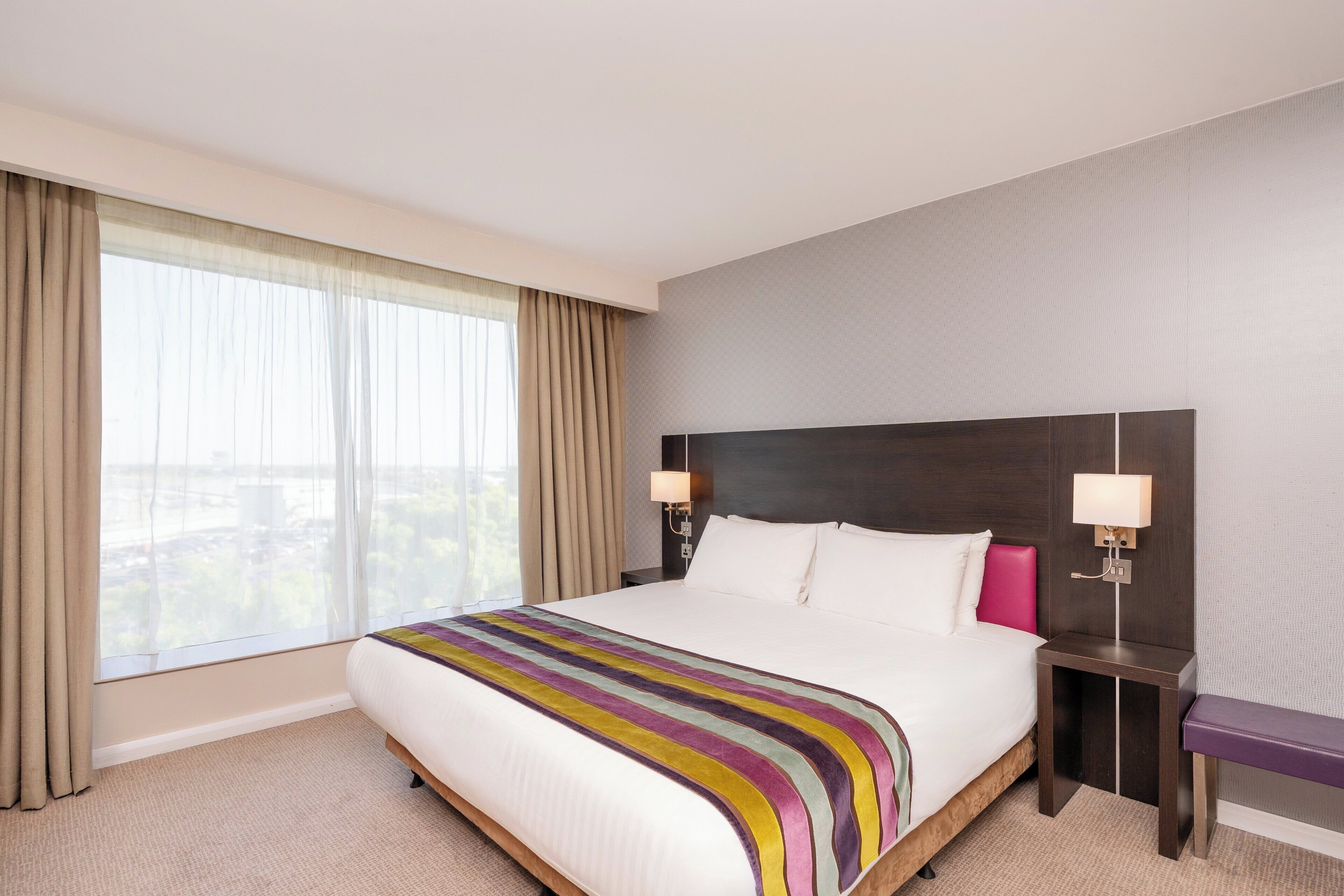 A hotel room with a large bed, a view of the city, and a nightstand with a lamp.